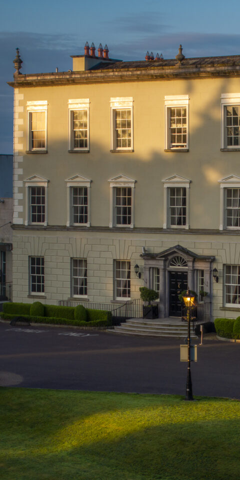 A luxurious hotel room with a large bed, elegant furniture, soft lighting, and calming neutral colors, featuring a window with drapes and bedside lamps for a cozy atmosphere.