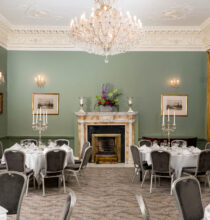 Elegant drawing room with plush seating, grand paintings, ornate decor, large windows, and warm lighting creating a cozy and inviting atmosphere. Ideal for relaxation or social gatherings.